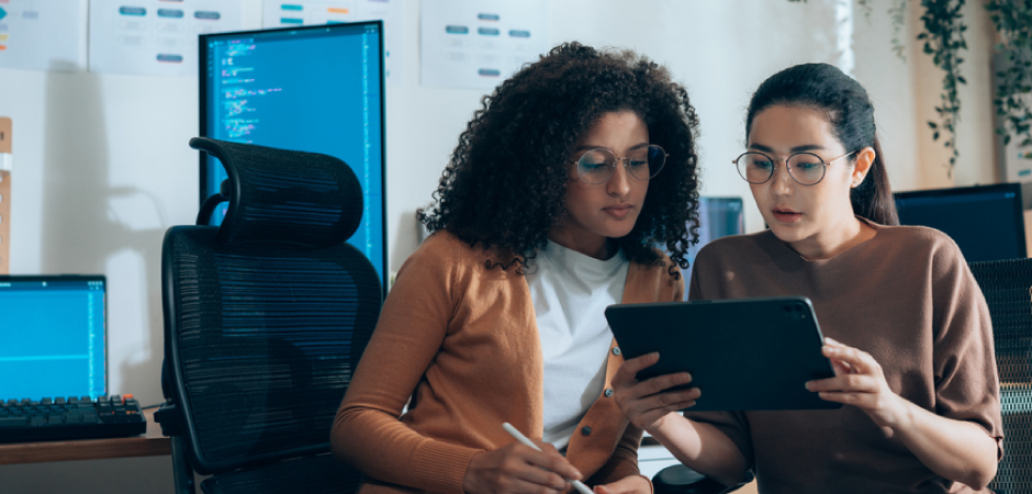 two women sitting and looking at a tablet.